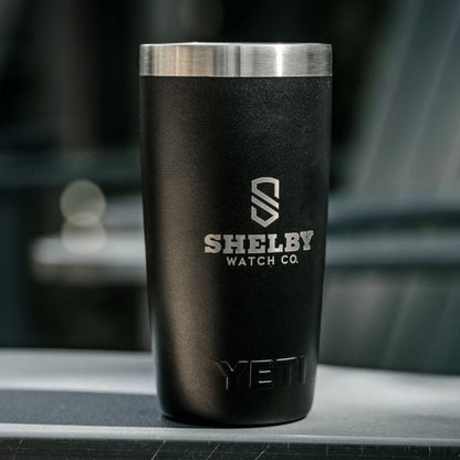 A matte black YETI travel tumbler with a brushed stainless steel rim, featuring the Shelby Watch Co. logo printed in silver on the front, set against a blurred dark background.